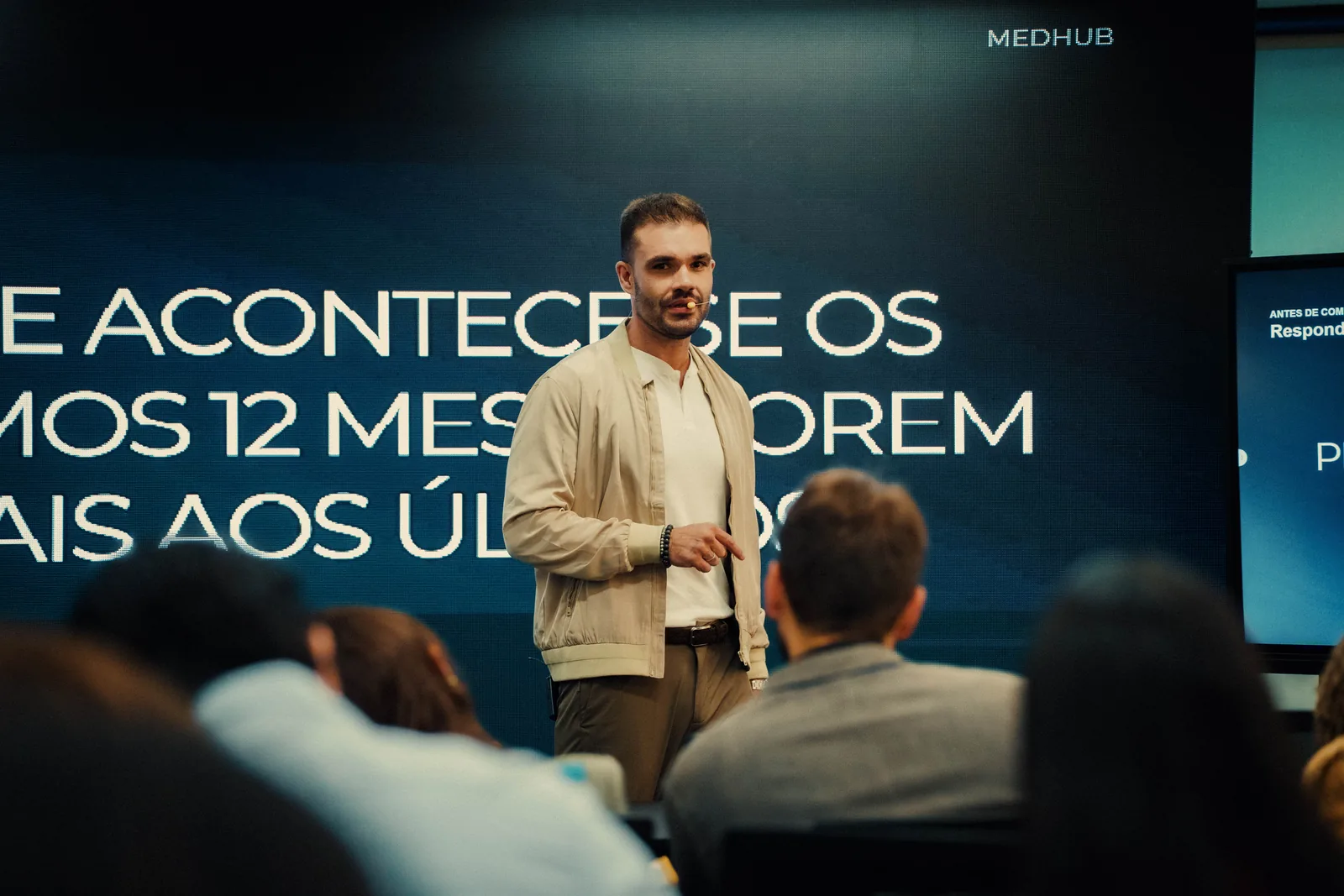Palestrante com microfone headset falando em frente ao painel de LED do MedHub